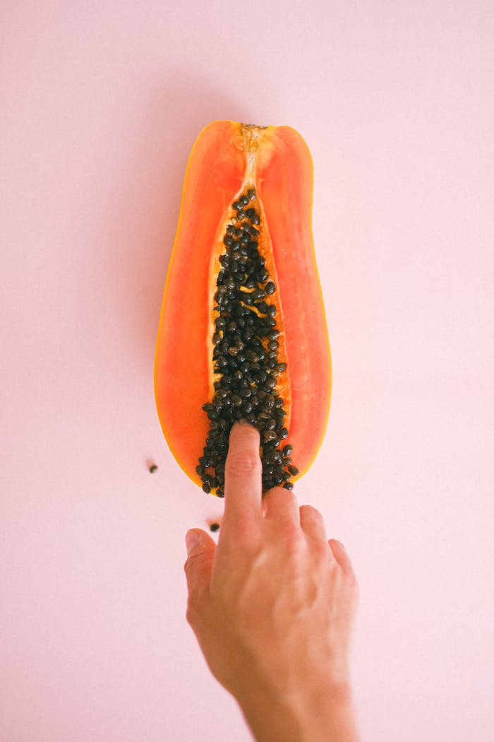 services-01 Hand interacting with a ripe papaya on a pink background, evoking playful and sensual themes.