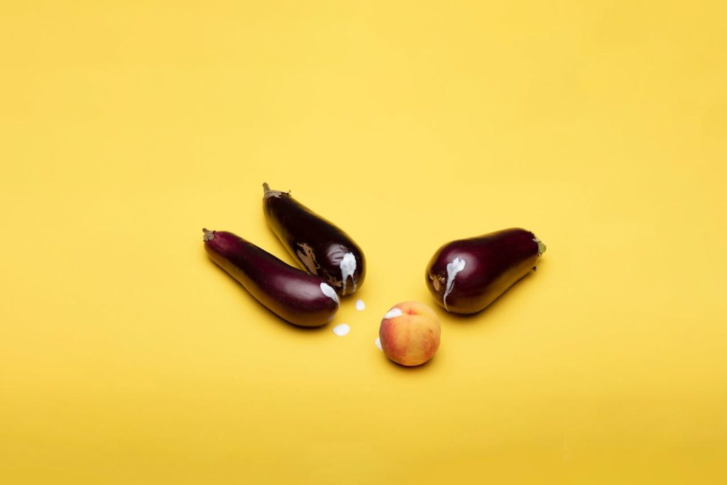 Playful composition with eggplants and peach on a vibrant yellow background.