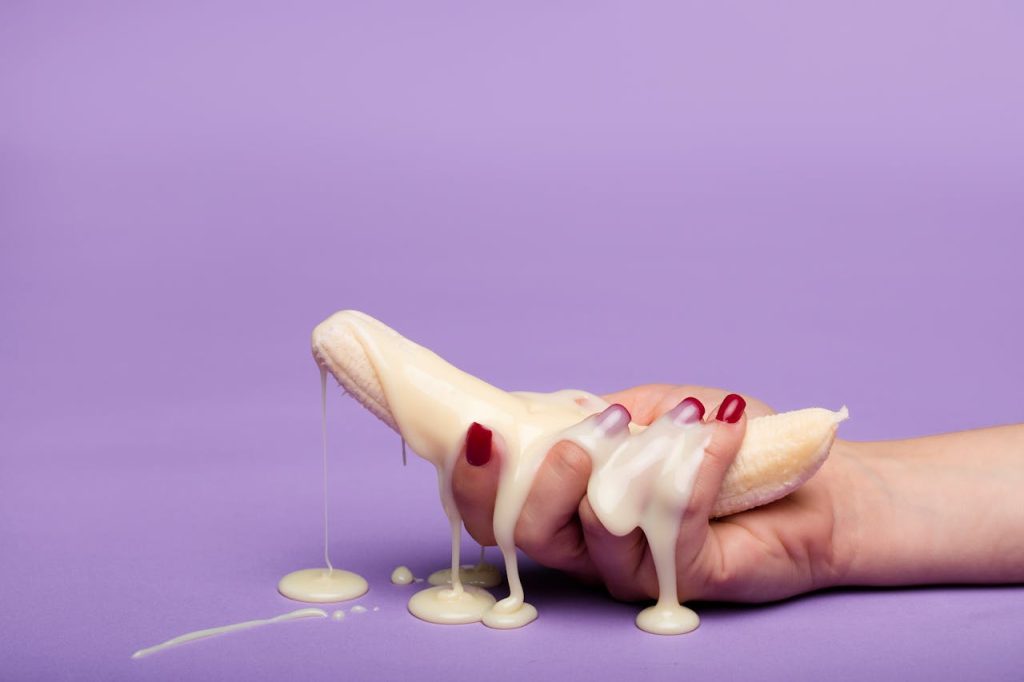 Creative conceptual image of a banana with cream on a purple backdrop, symbolizing indulgence.